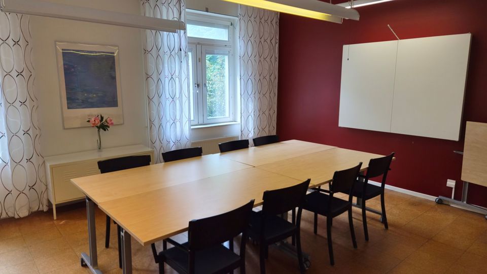 Ett mötesrum med fyra ihopskjutna skrivbord och åtta stolar.
