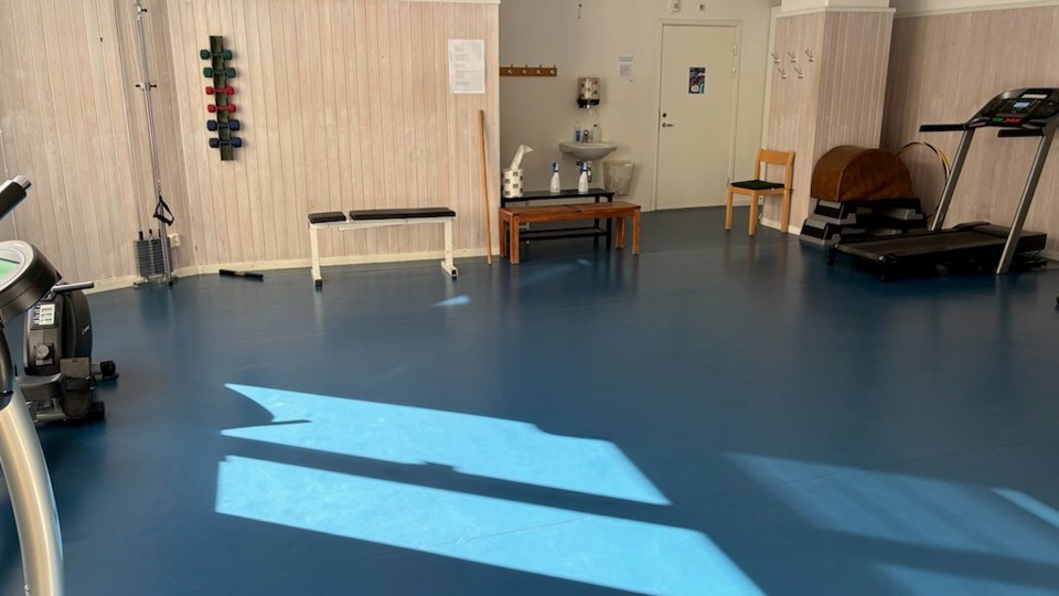 En gymnastiksal med golvyta, träningsredskap och ett handfat.