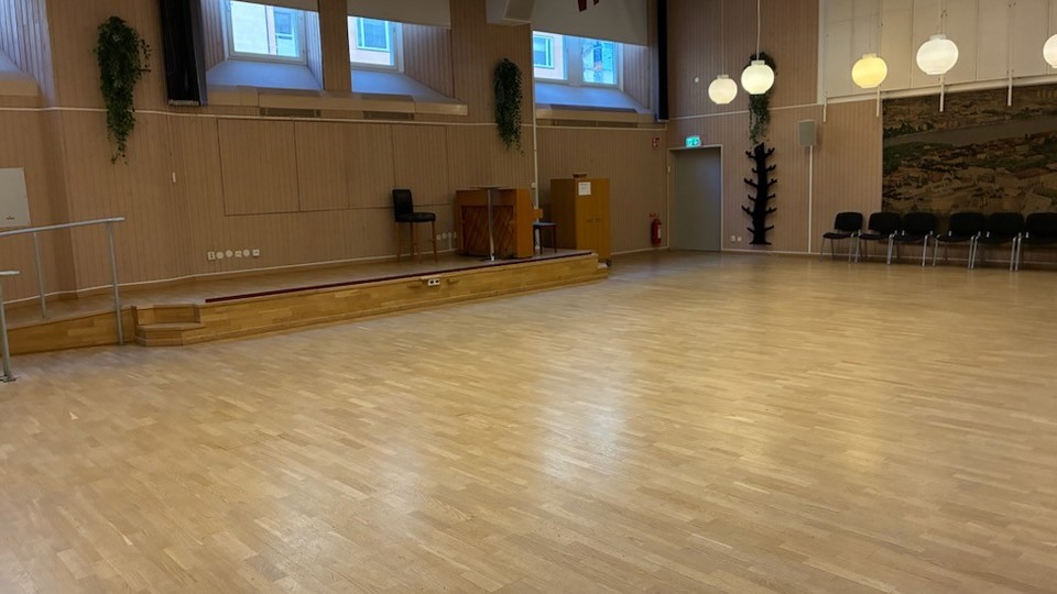 Ett stort rum med dansgolv och en liten scen. Stolar står längs med väggen.
