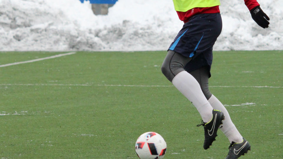 En person som spelar fotboll på en konstgräsplan med snöhögar runt omkring.