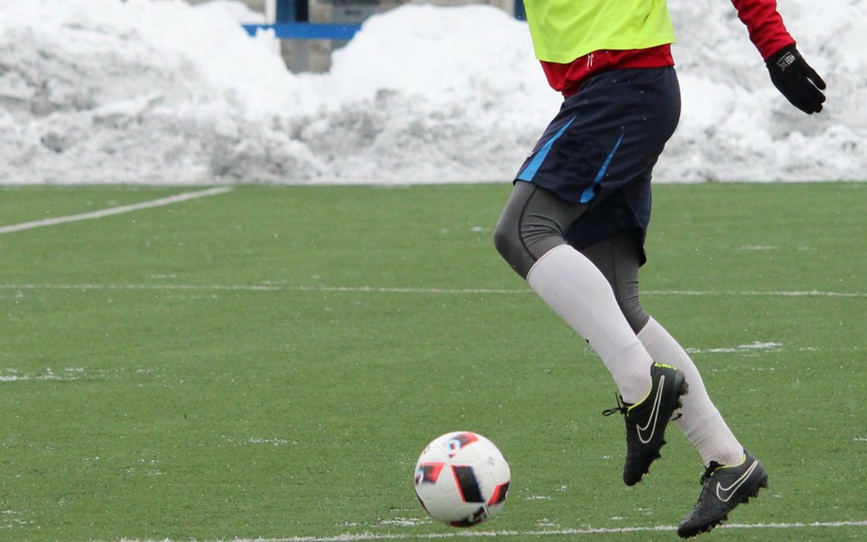En person som spelar fotboll på en konstgräsplan med snöhögar runt omkring.
